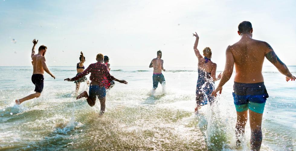 Ungdom hopper i havet en fin sommerdag.